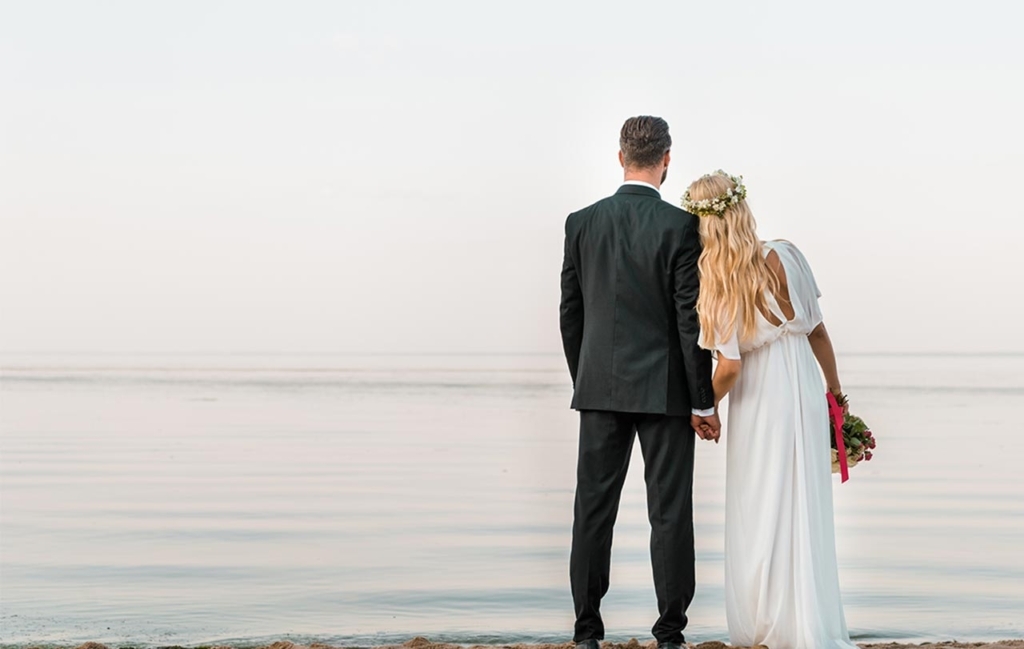 Decorative image for the wedding website design blog post: Bride and a groom by the water photo taken from back